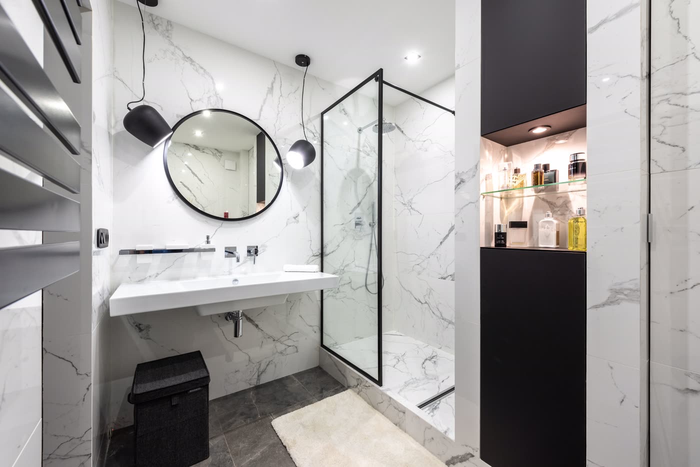 Monochrome bathroom renovation with marble-look tiling, a wall-hung basin, round black mirror and black-framed shower screen