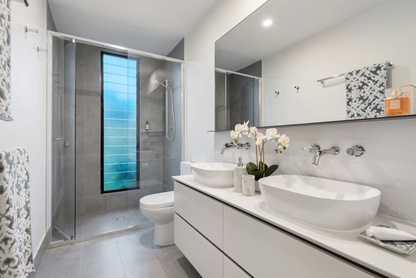 Bathroom renovation with twin vessel basins, wall-mounted tapware and a grey-tiled walk-in shower with a slot window