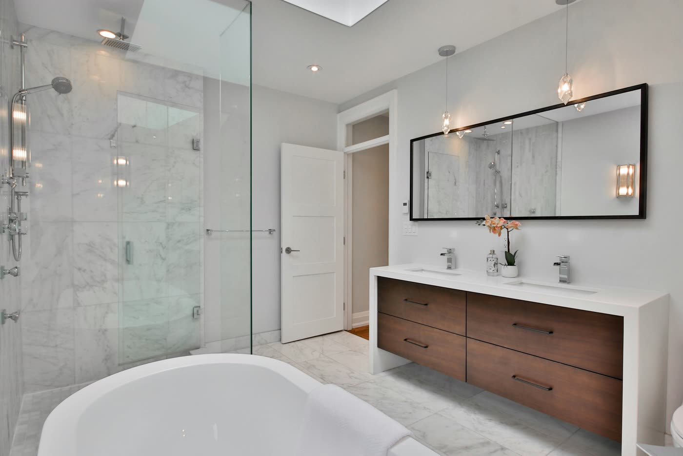 Bathroom renovation with a marble walk-in shower, floating walnut double vanity and a black-framed mirror under a skylight
