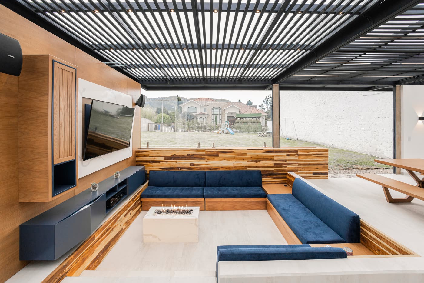 Covered outdoor living extension with a louvred roof, built-in banquette seating, timber feature wall and a fire table