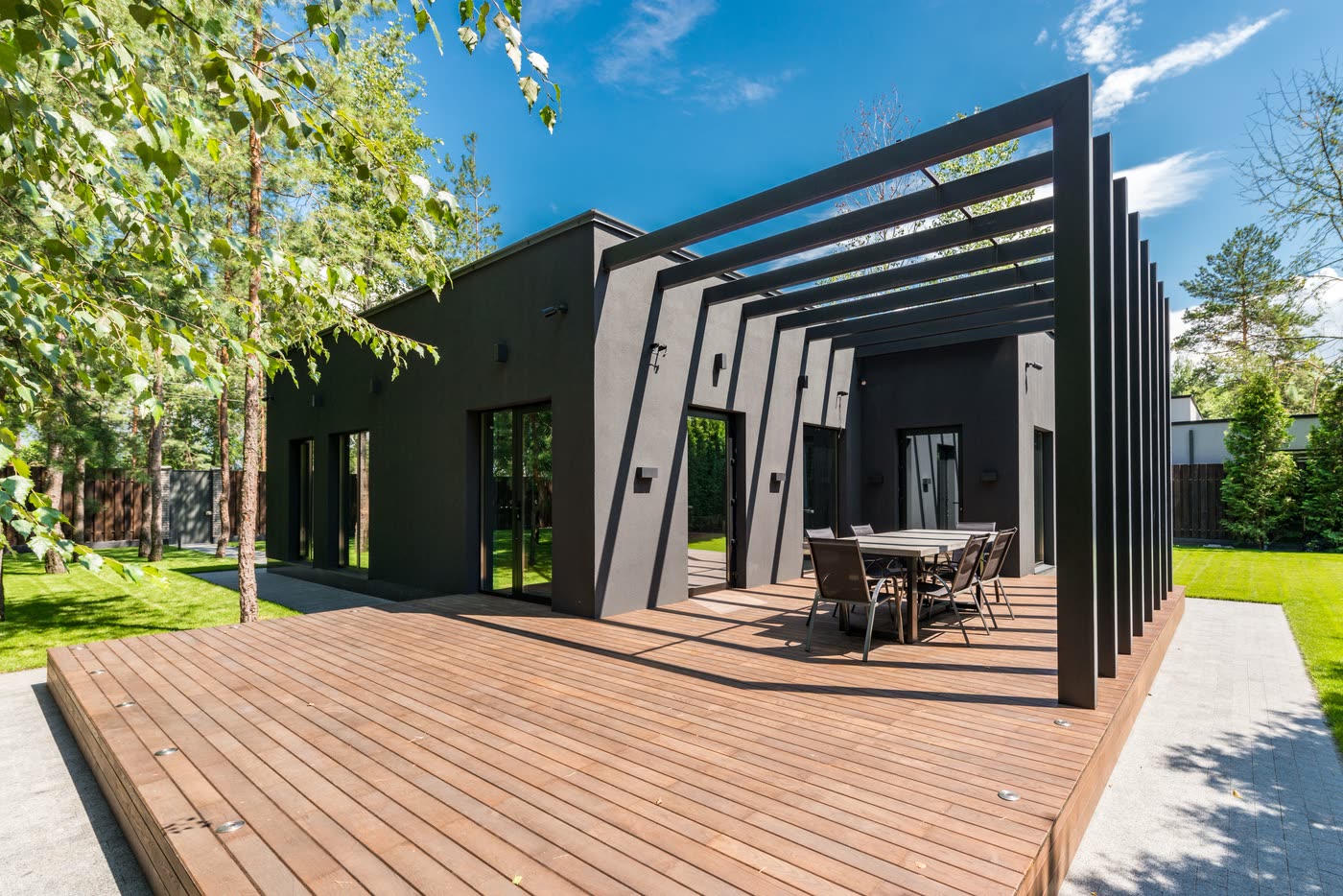 Rear home extension with charcoal rendered walls, full-height sliding doors, a battened pergola and a wide timber deck