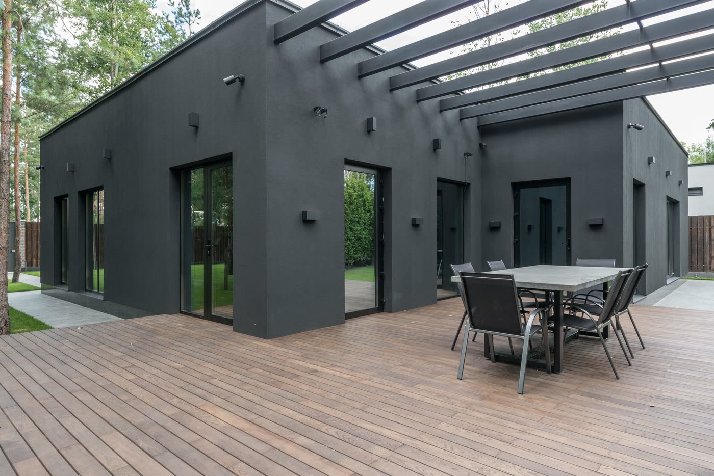 Home extension opening onto a timber deck through banks of sliding glass doors, with outdoor dining under a pergola