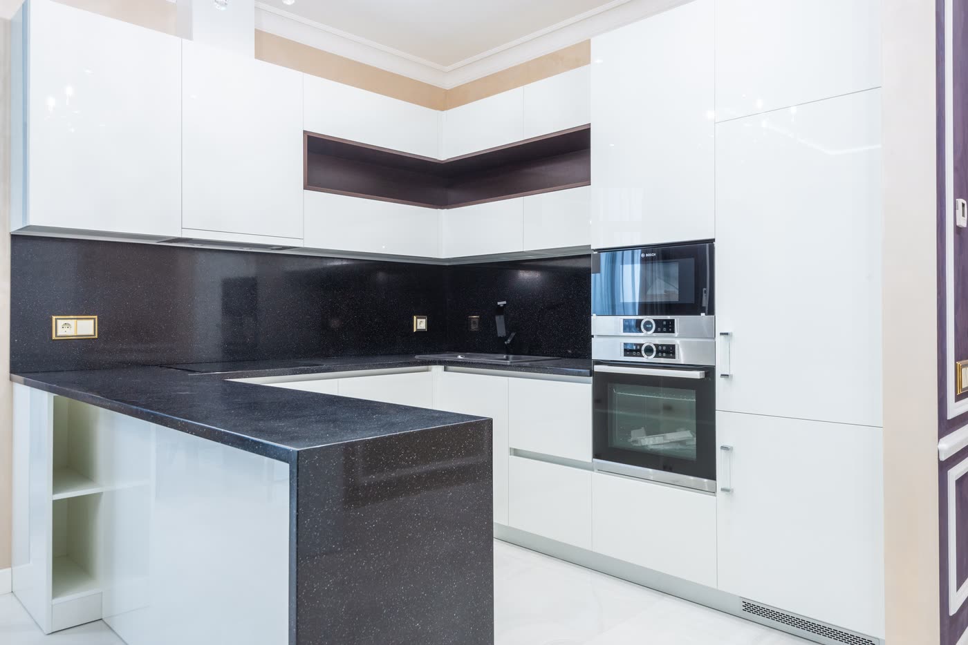 Compact kitchen renovation with handleless gloss white cabinetry, a dark stone benchtop and splashback, and built-in ovens