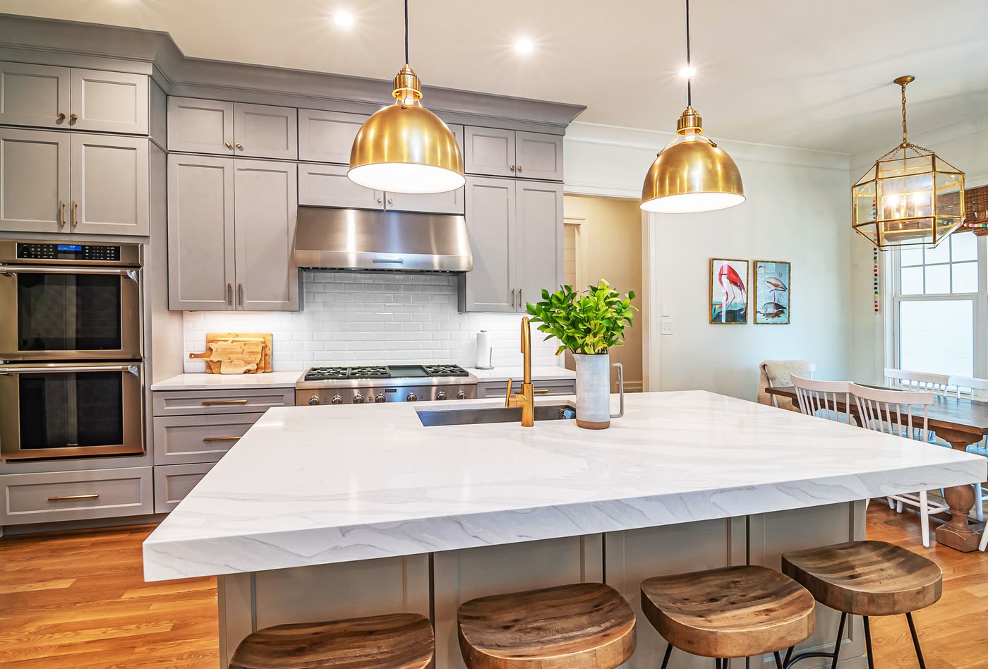 Kitchen renovation with a large marble waterfall island, grey shaker cabinetry, brass pendant lights and timber bar stools